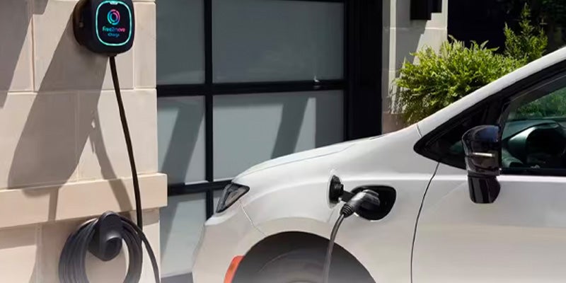 A white electric vehicle charging at a wall-mounted Free2move charger outside a building.