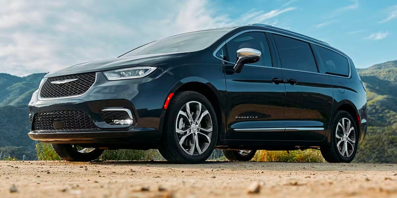 Black minivan parked outdoors on a gravel surface with mountains and sky in the background