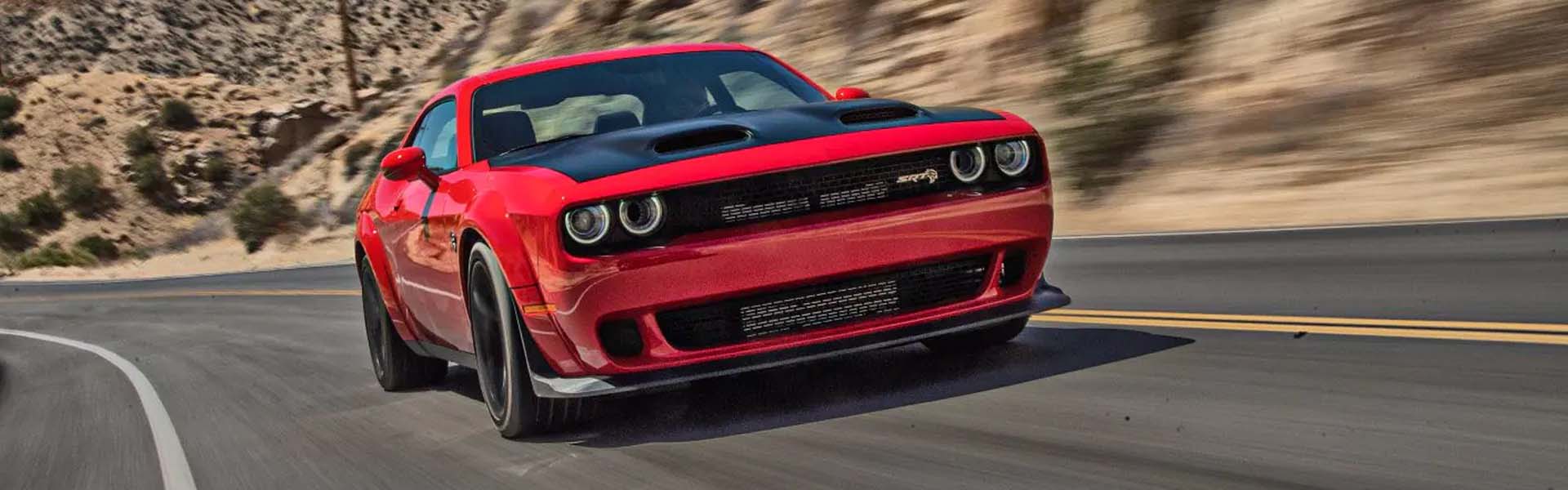 A red sports car with a black hood and black grille speeds along a winding desert road.