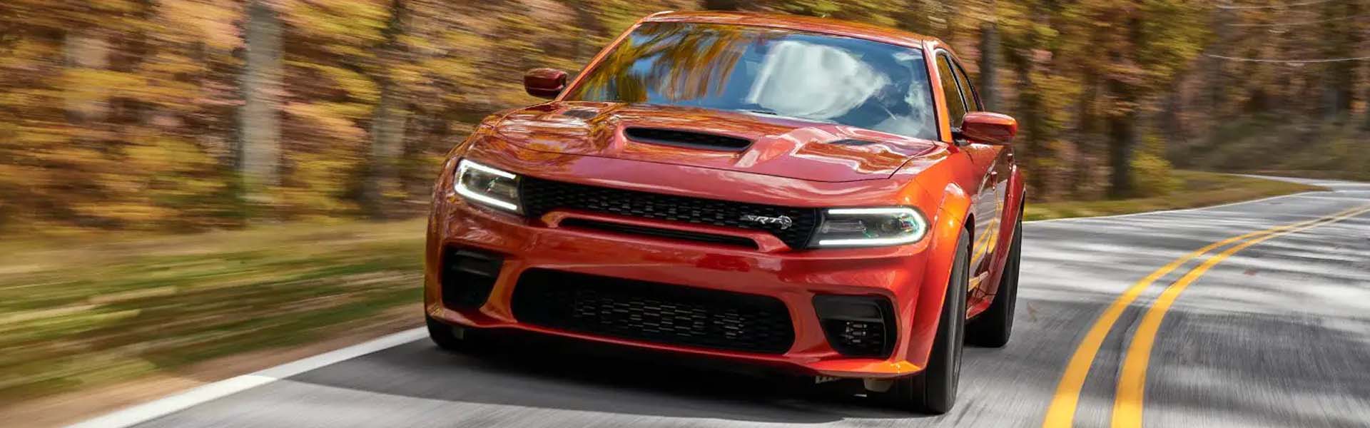 Red Dodge Charger SRT Hellcat Widebody driving quickly on a winding road bordered by blurred autumn trees.