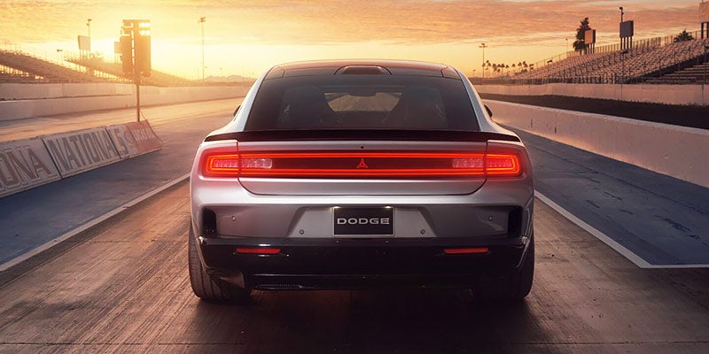Rear view of a silver Dodge sports car on a drag strip with its red taillights illuminated at sunset.