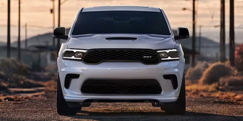 Front view of a white Dodge Durango SRT SUV with black grille and headlights, parked on a dirt road.