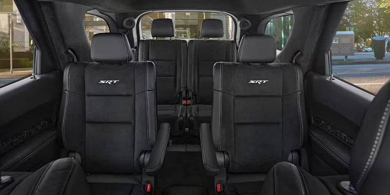 Interior of a vehicle featuring black leather seating with SRT logos and white stitching, looking towards the back.