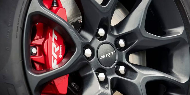 Close-up of a dark gray multi-spoke car wheel with silver lug nuts, showing a red Brembo SRT brake caliper.