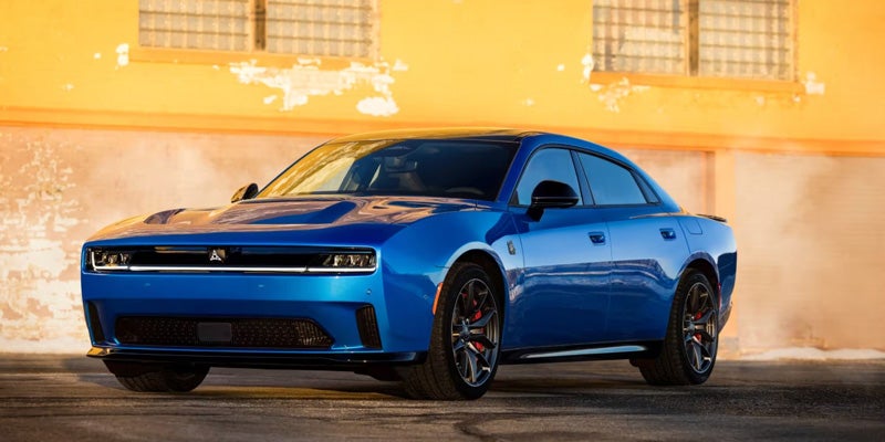 A blue electric Dodge Charger Daytona Scat Pack, viewed from a low angle, shines against a yellow wall.