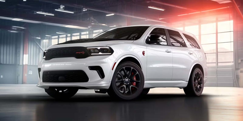 A white Dodge Durango SRT Hellcat SUV with a black hood and wheels, parked inside a modern garage.