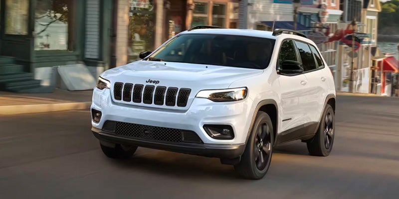 White Jeep Cherokee SUV driving on a city street with storefronts and buildings in the background