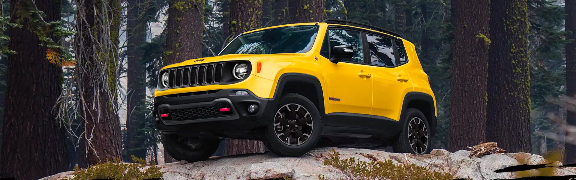 Bright yellow Jeep Renegade SUV parked on a rocky terrain with tall evergreen trees in the background.