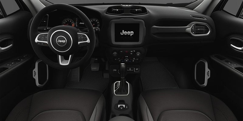 Interior view of a dark Jeep dashboard, steering wheel with Jeep logo, touch screen, and center console.