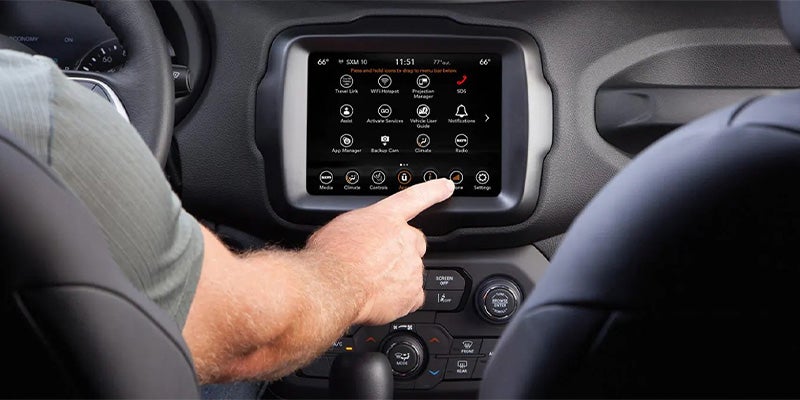 A person's hand reaches to touch the "Apps" icon on a car's infotainment touchscreen.