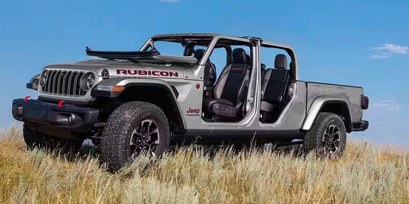 A silver Jeep Gladiator pickup truck, with doors and roof removed, parked in a field of dry grass.