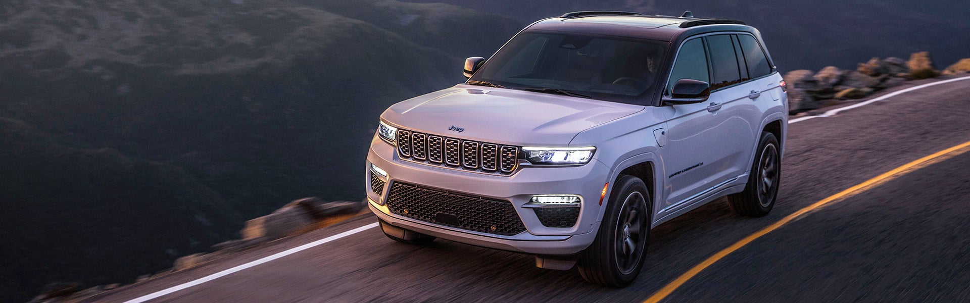 White Jeep Grand Cherokee L 4xe drives on a winding mountain road with an overcast sky.