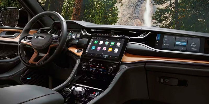 The interior of a vehicle with a large touchscreen display, wooden trim, and a mountain waterfall background.