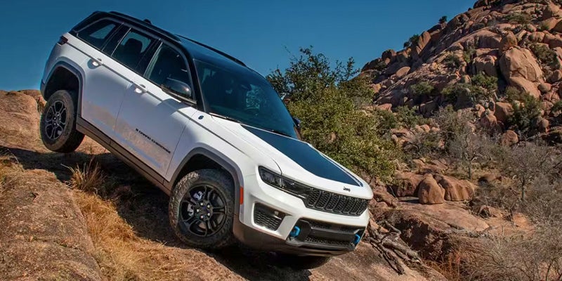 White Jeep Grand Cherokee 4xe off-roading up a rocky hill, with a black roof and hood stripe.