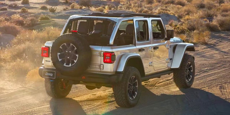 Rear view of a silver lifted Jeep Wrangler driving on a dusty desert road at sunset.
