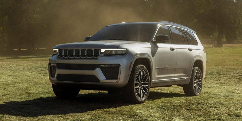 A silver Jeep Grand Cherokee Laredo parked on a grassy field with trees in the hazy background.