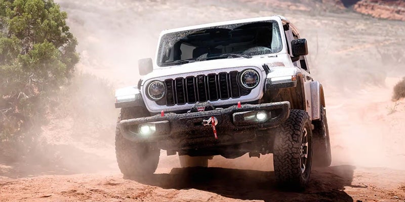White Jeep Wrangler off-road vehicle driving through a dusty desert trail