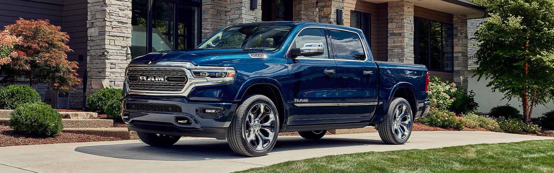 Navy blue 2023 Ram 1500 truck parked on a driveway in front of a modern stone house with landscaping.