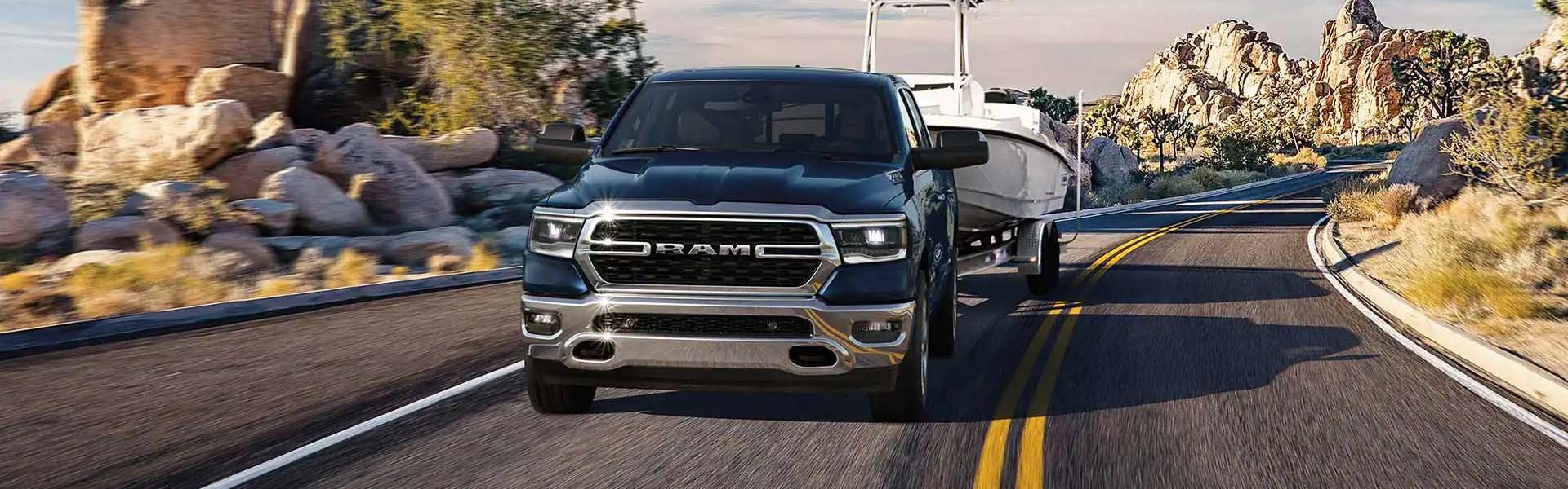 A dark blue Ram pickup truck pulls a white boat on a trailer down a desert highway, surrounded by rock formations.