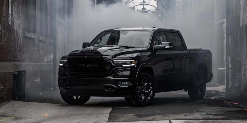 A black Ram pickup truck with headlights on, emerging from a smoky, dimly lit urban alleyway.