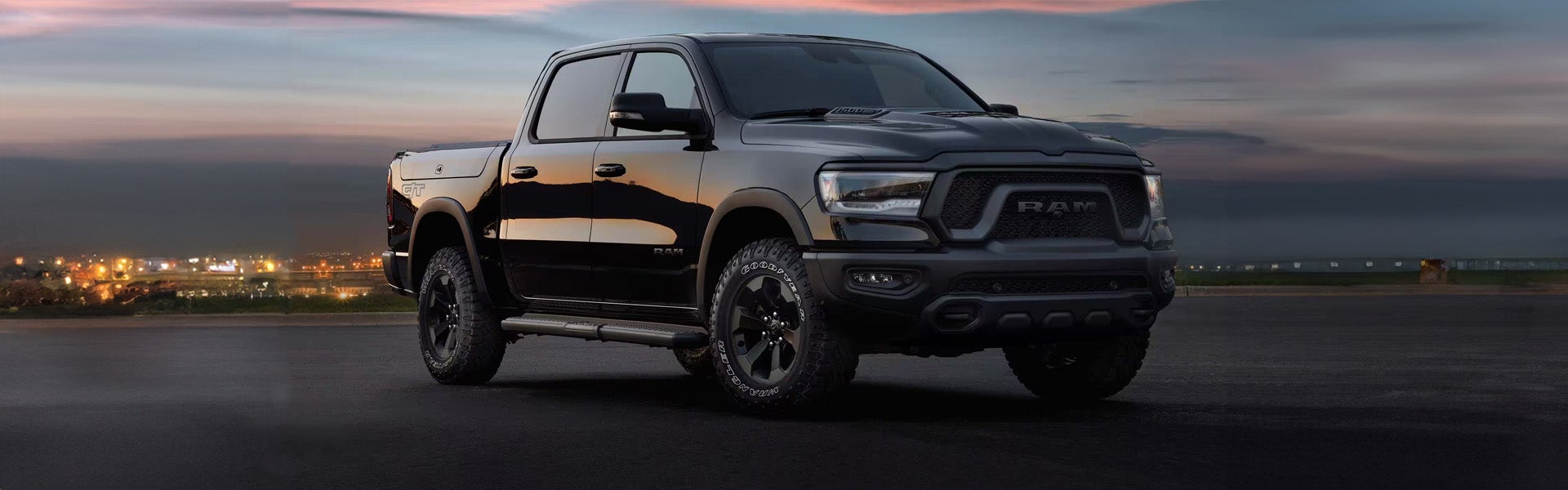 A black Ram pickup truck angled right, with a dark city skyline in the background at dusk.