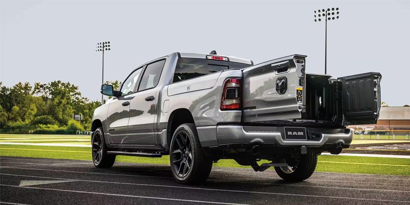 Silver Ram truck with an open tailgate and two side-swinging doors, viewed from the rear on a running track.