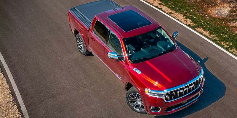Aerial view of a shiny red Ram pickup truck with a black sunroof and bed cover on an asphalt road.