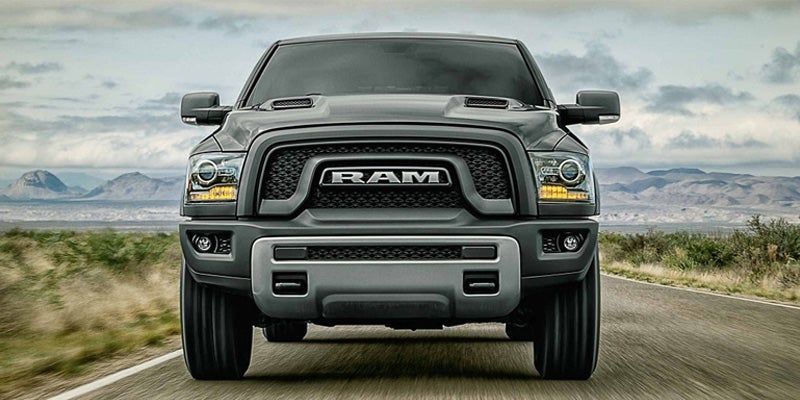 Front view of a dark gray Ram pickup truck driving on a rural road with mountains in the background.