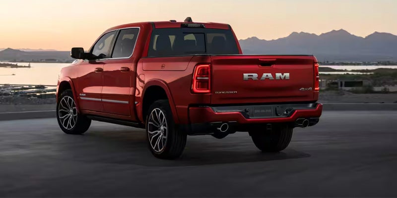 Rear view of a red Ram pickup truck with a large RAM logo on the tailgate, parked by a lake at sunset.