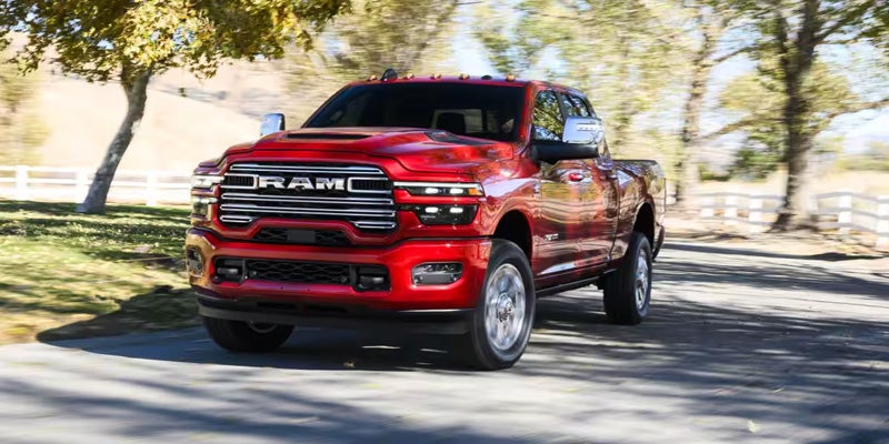 A shiny red Ram truck driving fast down a tree-lined road on a bright, sunny day.