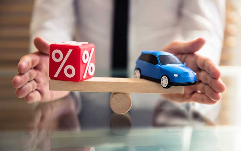 Model car and percentage symbol balanced on a wooden scale, representing auto loan interest rates and vehicle financing