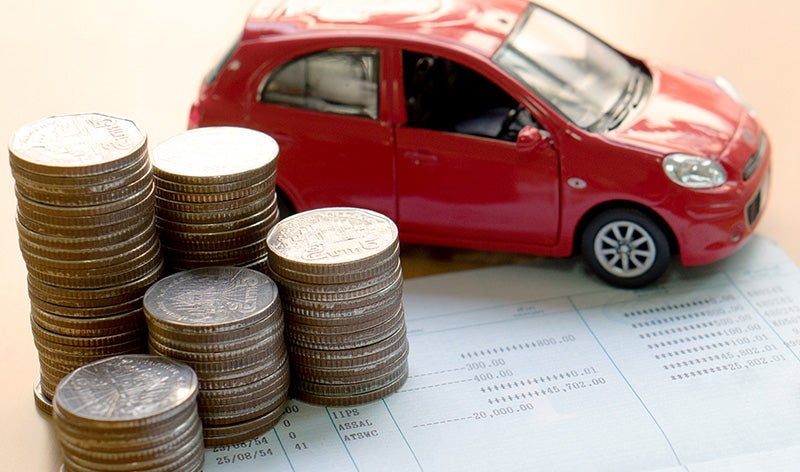 Red car model displayed beside stacks of coins on financial documents, representing car financing, vehicle costs, or auto loan planning