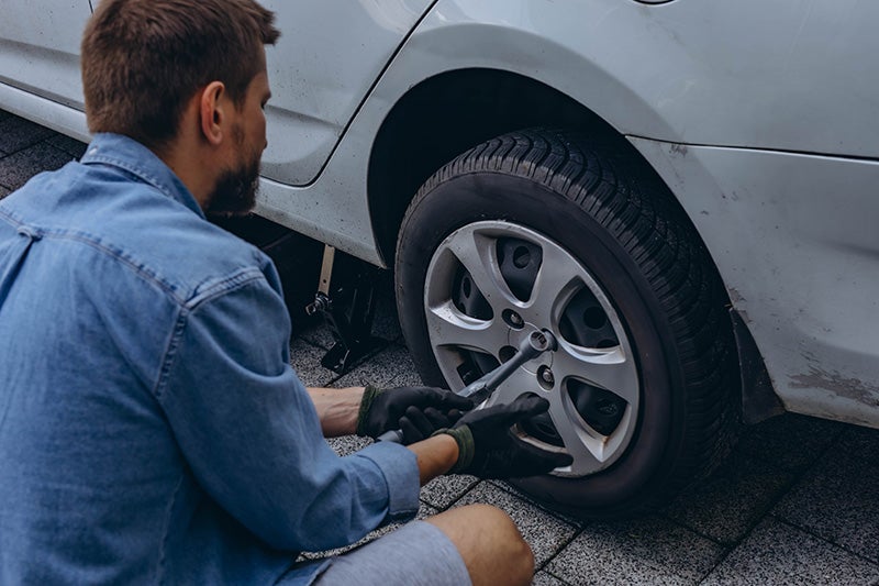 Person using a lug wrench to tighten or loosen wheel nuts while changing a tire on a parked vehicle