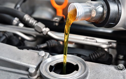 Close-up of fresh engine oil being poured into a vehicle's engine through the oil filler opening during routine maintenance