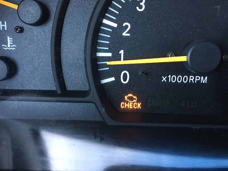 Technician using a dipstick to check engine oil level under the hood of a vehicle during routine maintenance