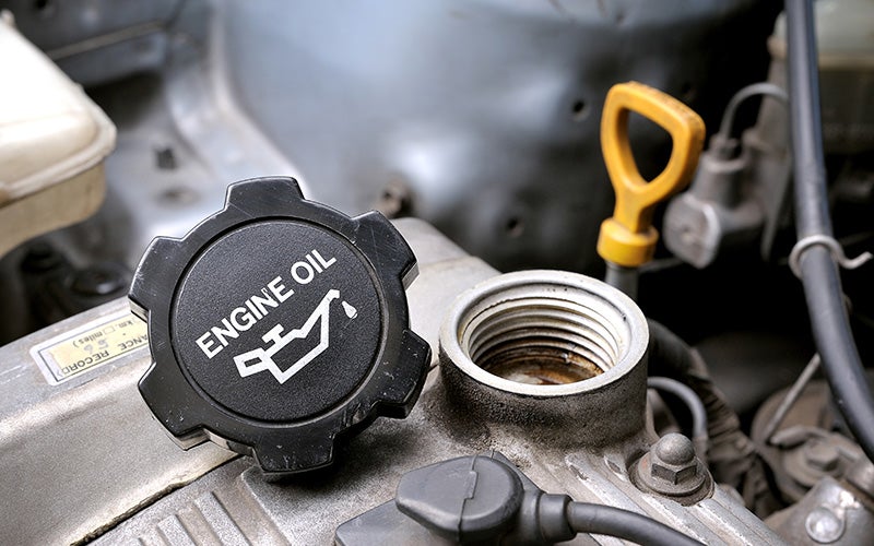 Engine oil cap and open oil filler neck on a vehicle engine, highlighting an oil change or engine maintenance service