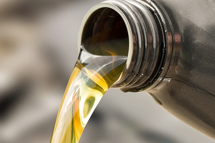 Close-up of golden motor oil being poured from the spout of a black plastic container
