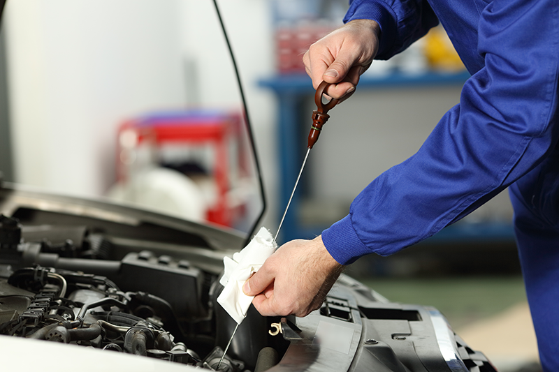 Close-up of a mechanic checking engine oil with a dipstick under the open hood of a vehicle during maintenance