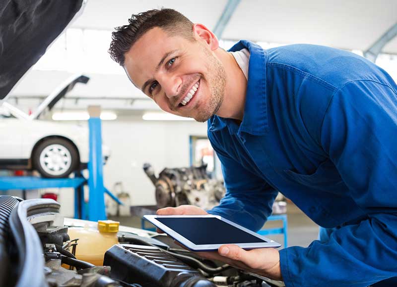 Automotive technician using a tablet while inspecting a vehicle engine in a repair shop